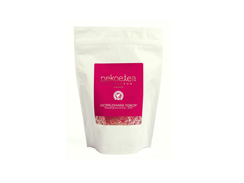 A white resealable pouch of Gopaldhara TGBOP second flush Darjeeling pekoe tea with a pink label and gold foil detailing