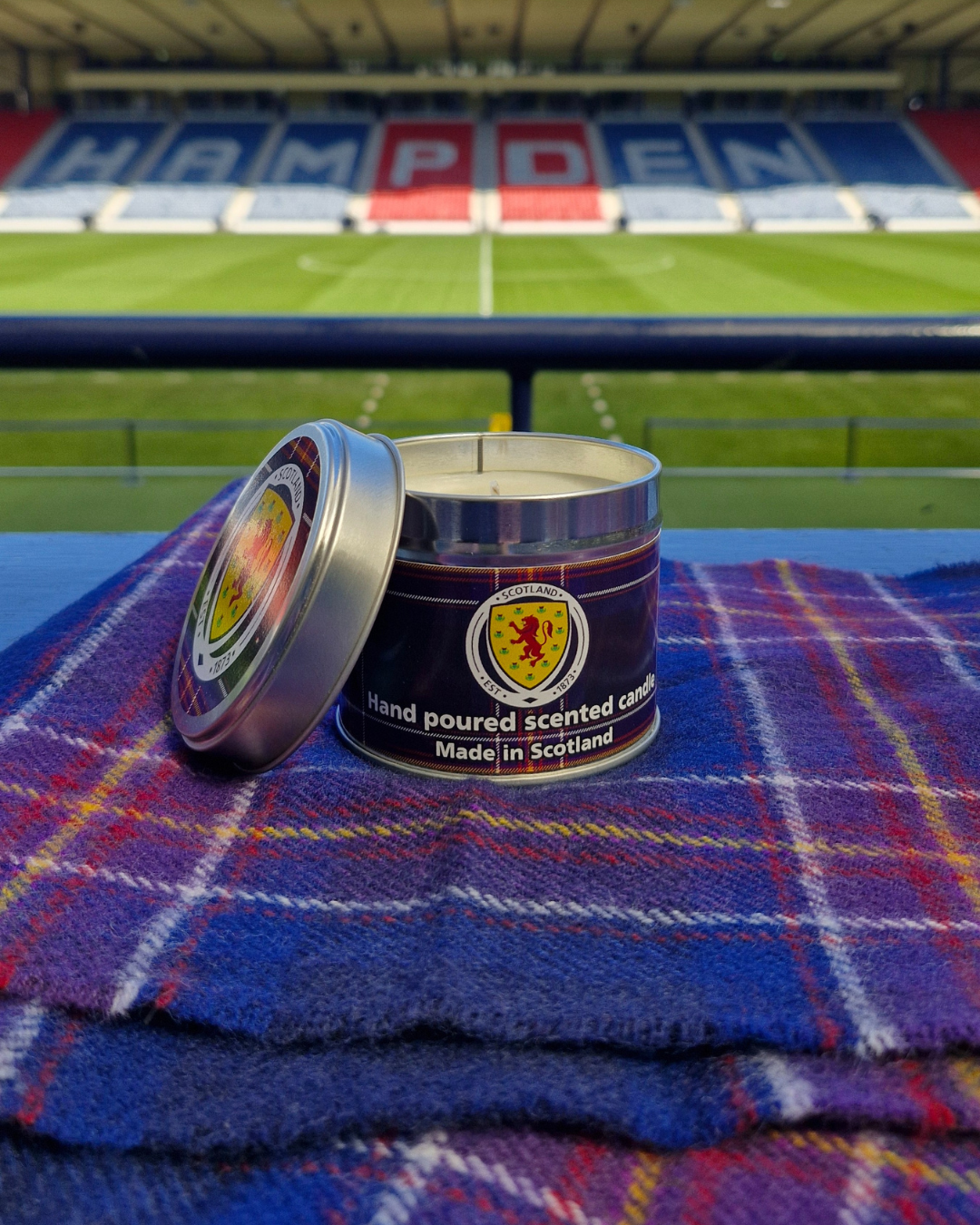 A hand-poured scented candle in a metallic tin featuring red and blue tartan and the Scottish national emblem