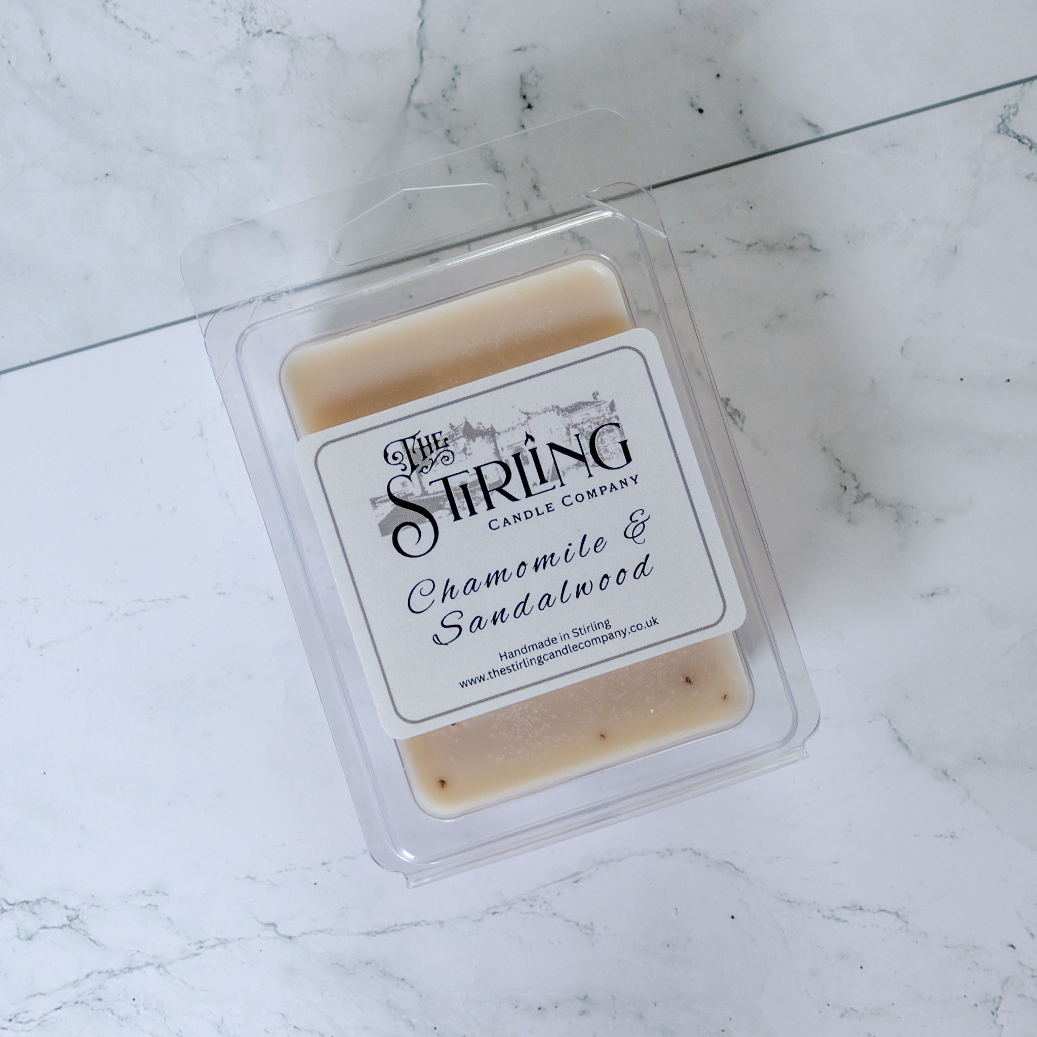 A beige chamomile and sandalwood wax melt clamshell in a clear plastic container from Stirling Candle Company