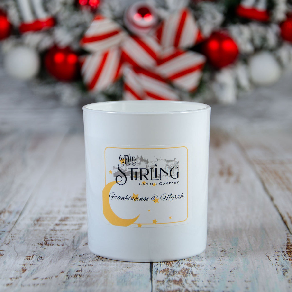 White candle with a label reading "The Stirling Candle Company" and "Frankincense & Myrrh" on a wooden surface with festive
