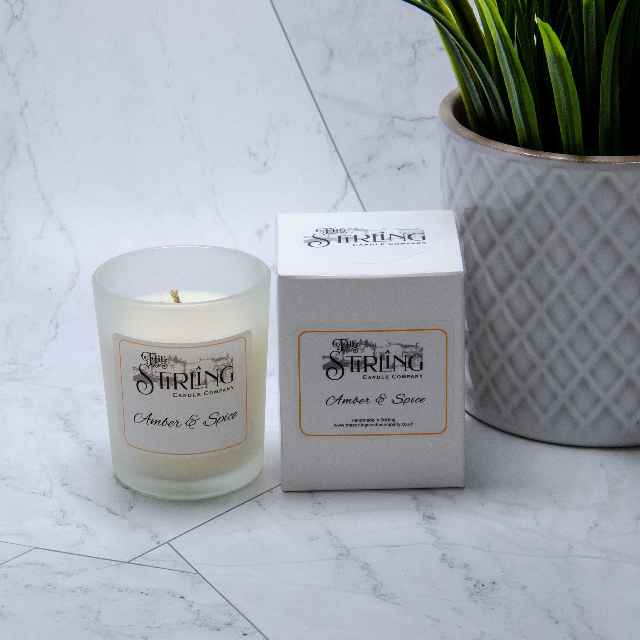 A frosted glass small candle with white wax and amber and spice scent in a clear cylindrical container from string candle company