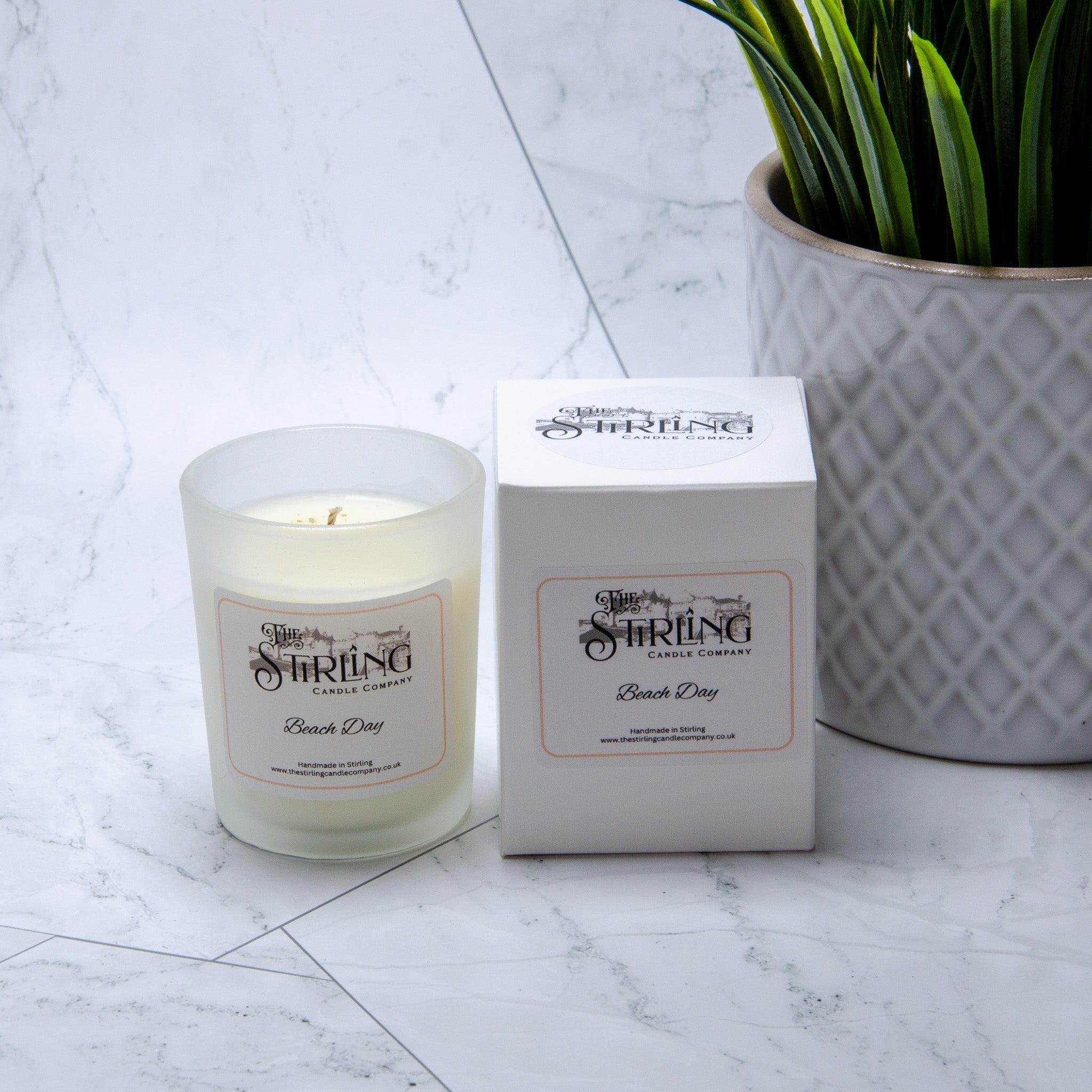 A frosted glass small candle with white wax from the stirling candle company labeled beach day with matching box