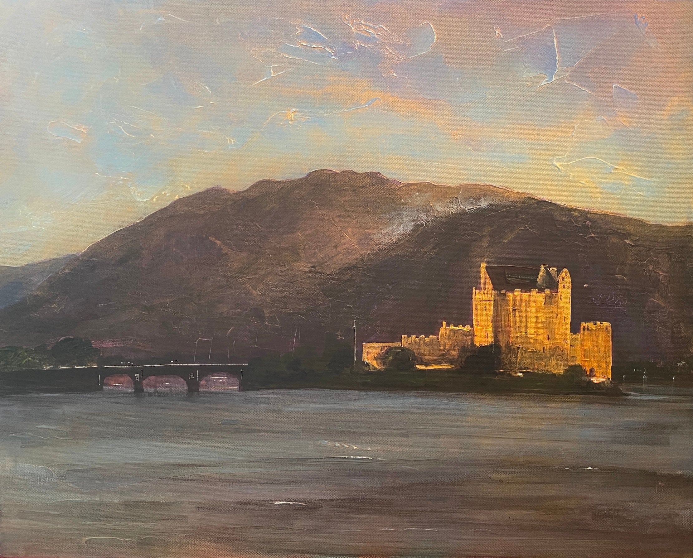 Eilean Donan Castle glowing at sunset on a lake with mountains and a bridge in the background