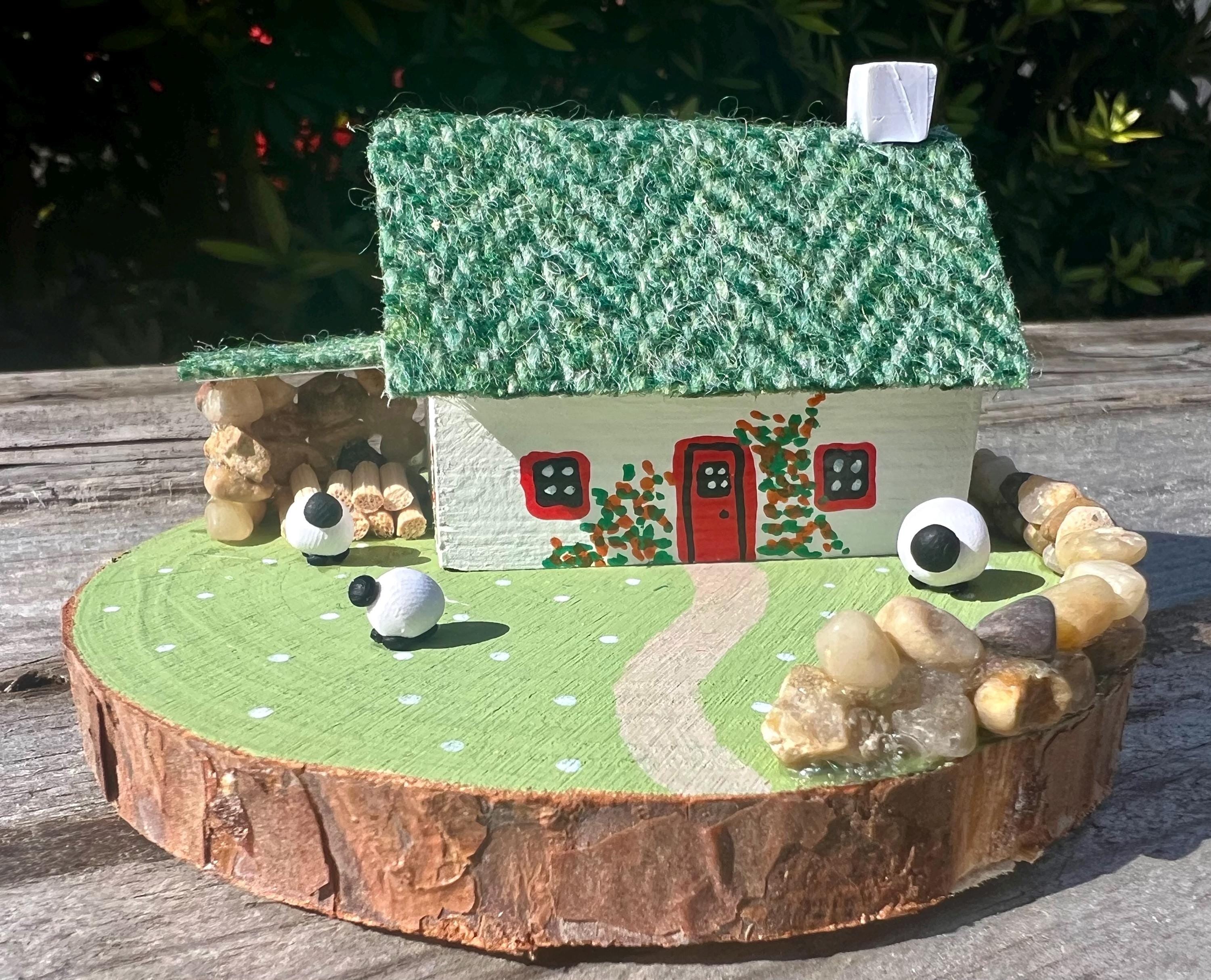 Miniature Irish cottage with green herringbone roof, red door, sheep, and stone wall