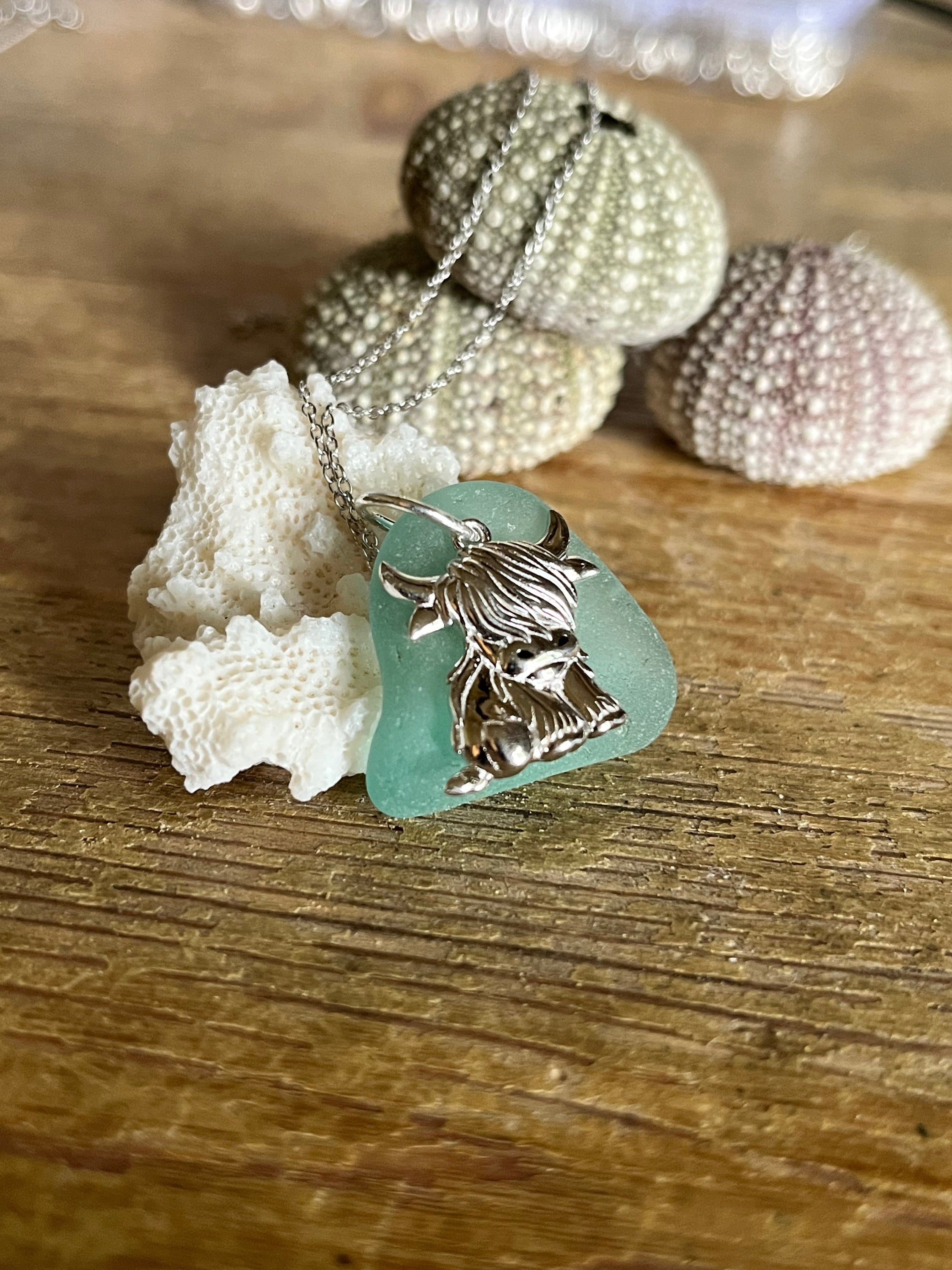 Delicate 925 silver highland cow pendant on chain over turquoise sea glass