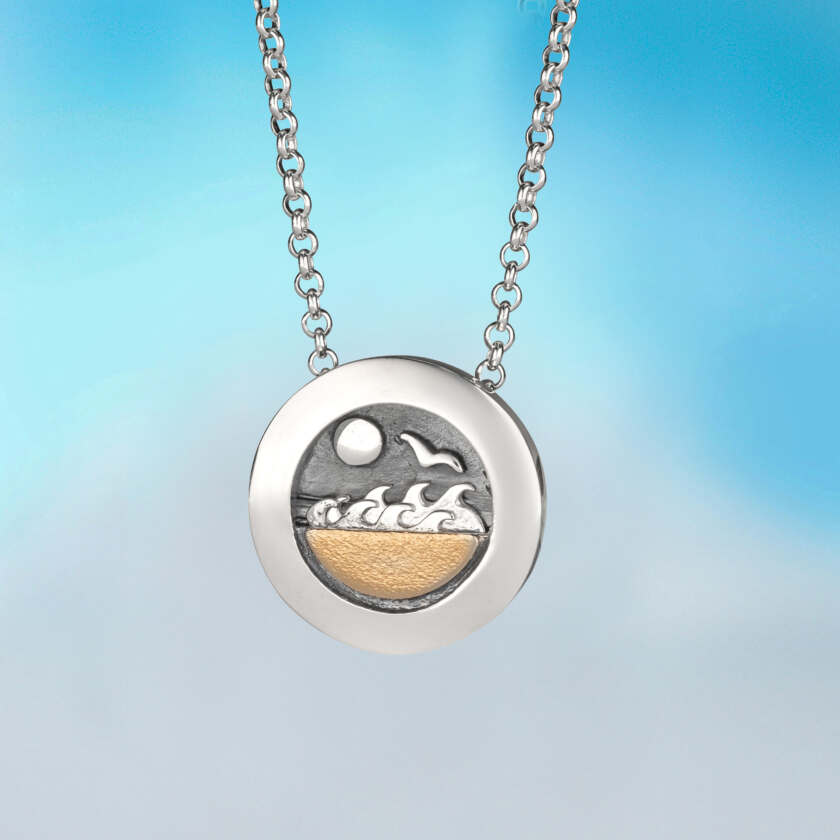 Silver pendant necklace named Making Waves pendant with circular two-tone silver and gold beach scene engraving