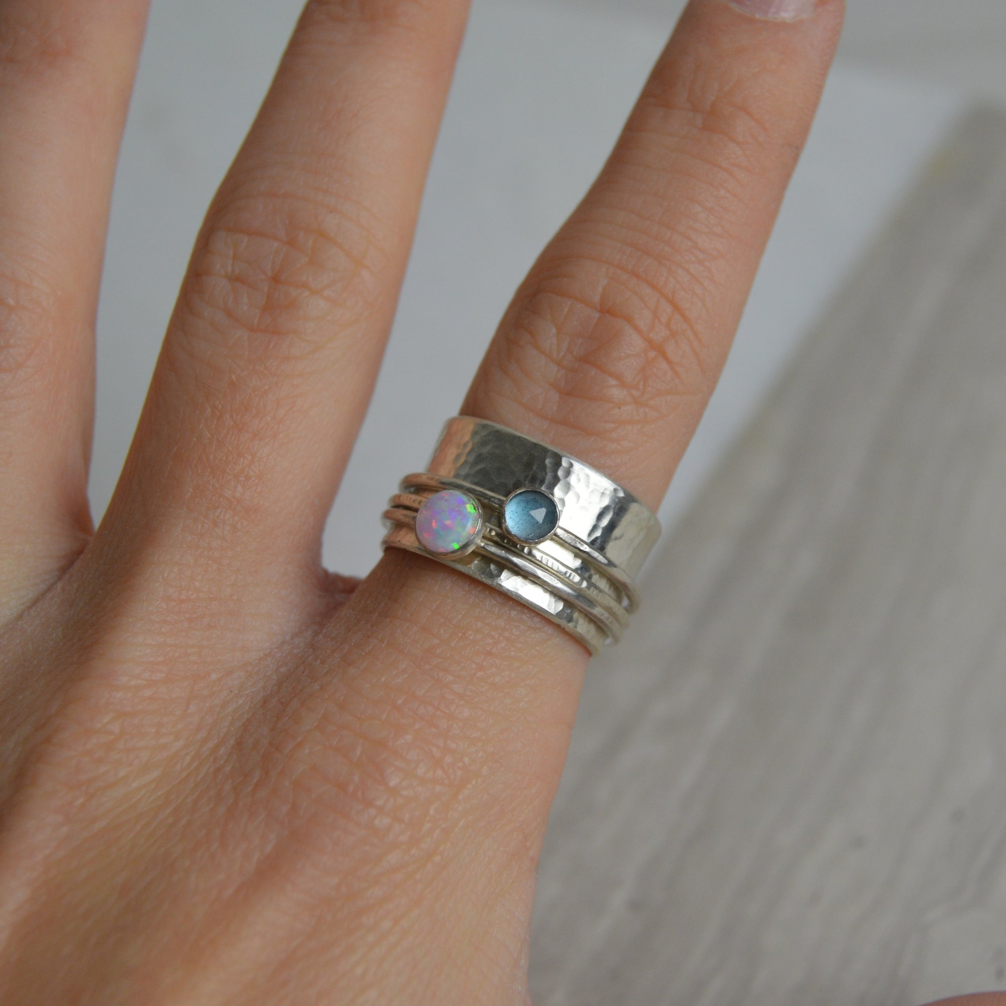 A stack of silver opal and topaz spinning rings with hammered texture and iridescent gemstones set in the center
