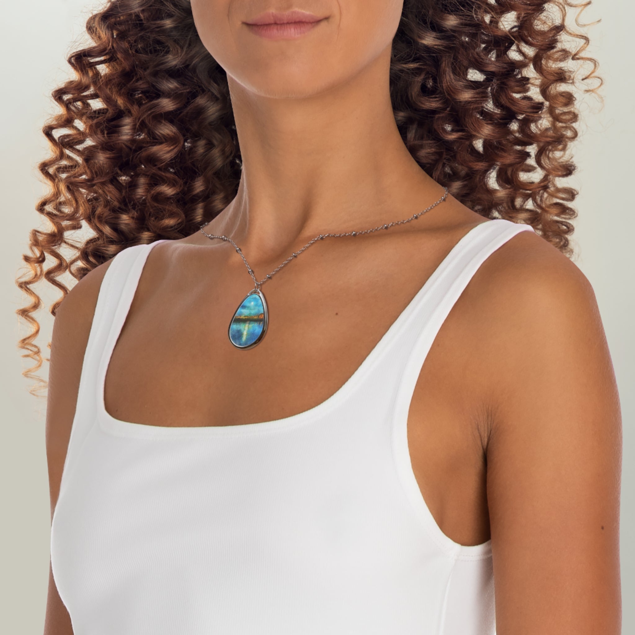 Woman with curly brown hair wearing a white tank top and blue green teardrop pendant necklace