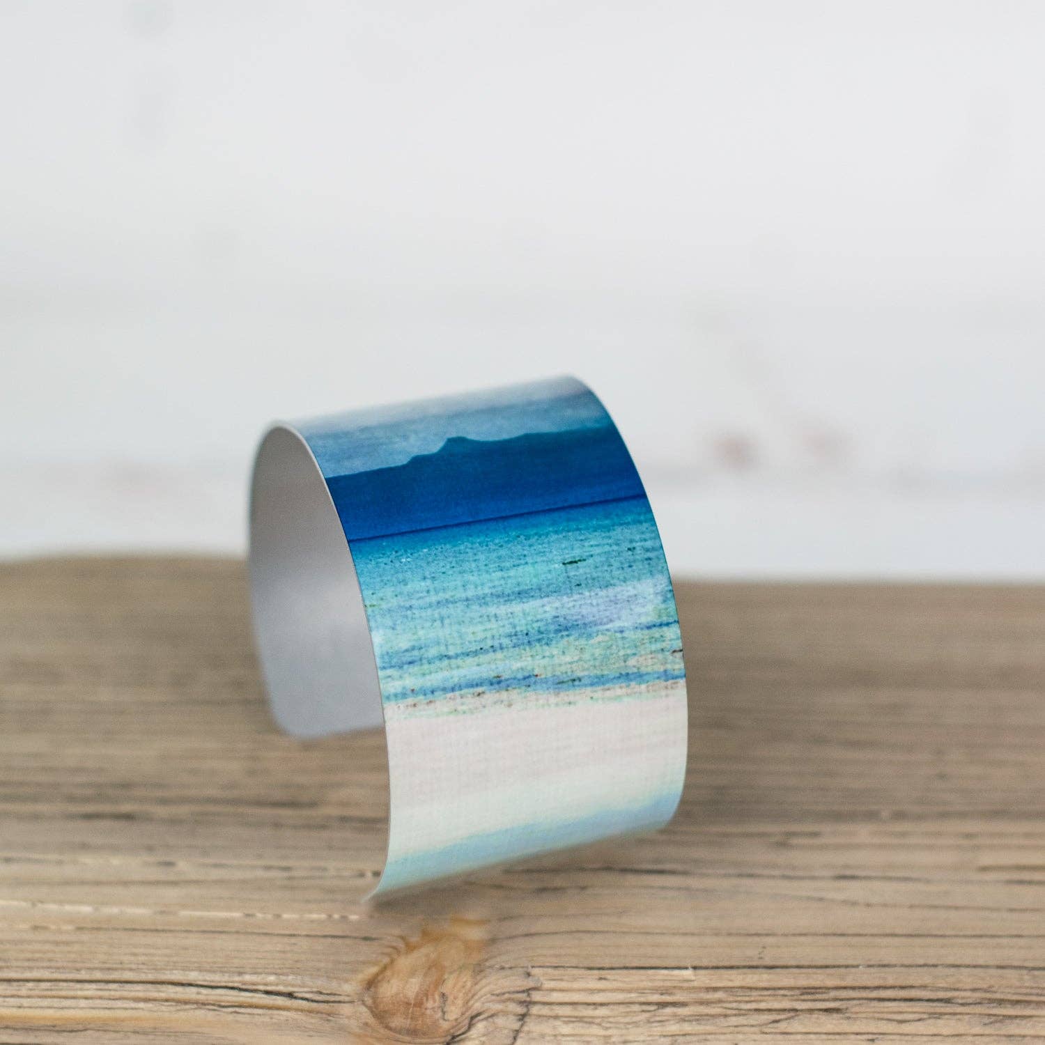 A sleek aluminum cuff bracelet from applecross featuring a vibrant ocean scene with blues and turquoise waves