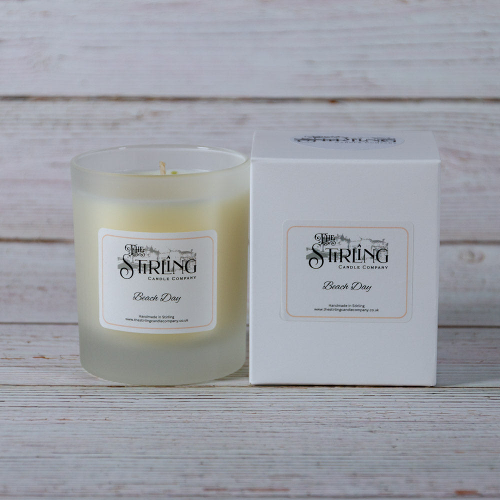 A frosted glass medium candle jar with pale yellow wax and a white beach day label from Stirling Candle Company