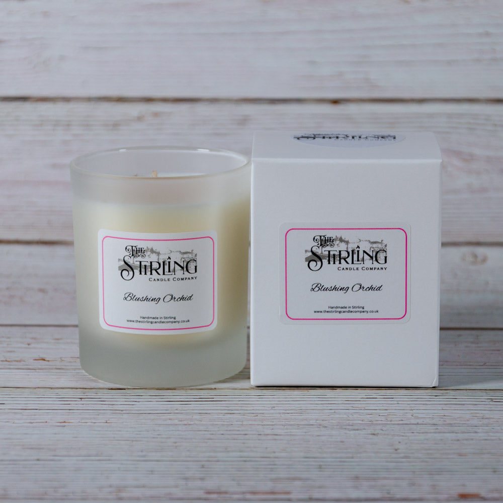 A frosted glass medium candle jar with creamy white wax and a pink bordered blushing orchid label from Stirling Candle Company