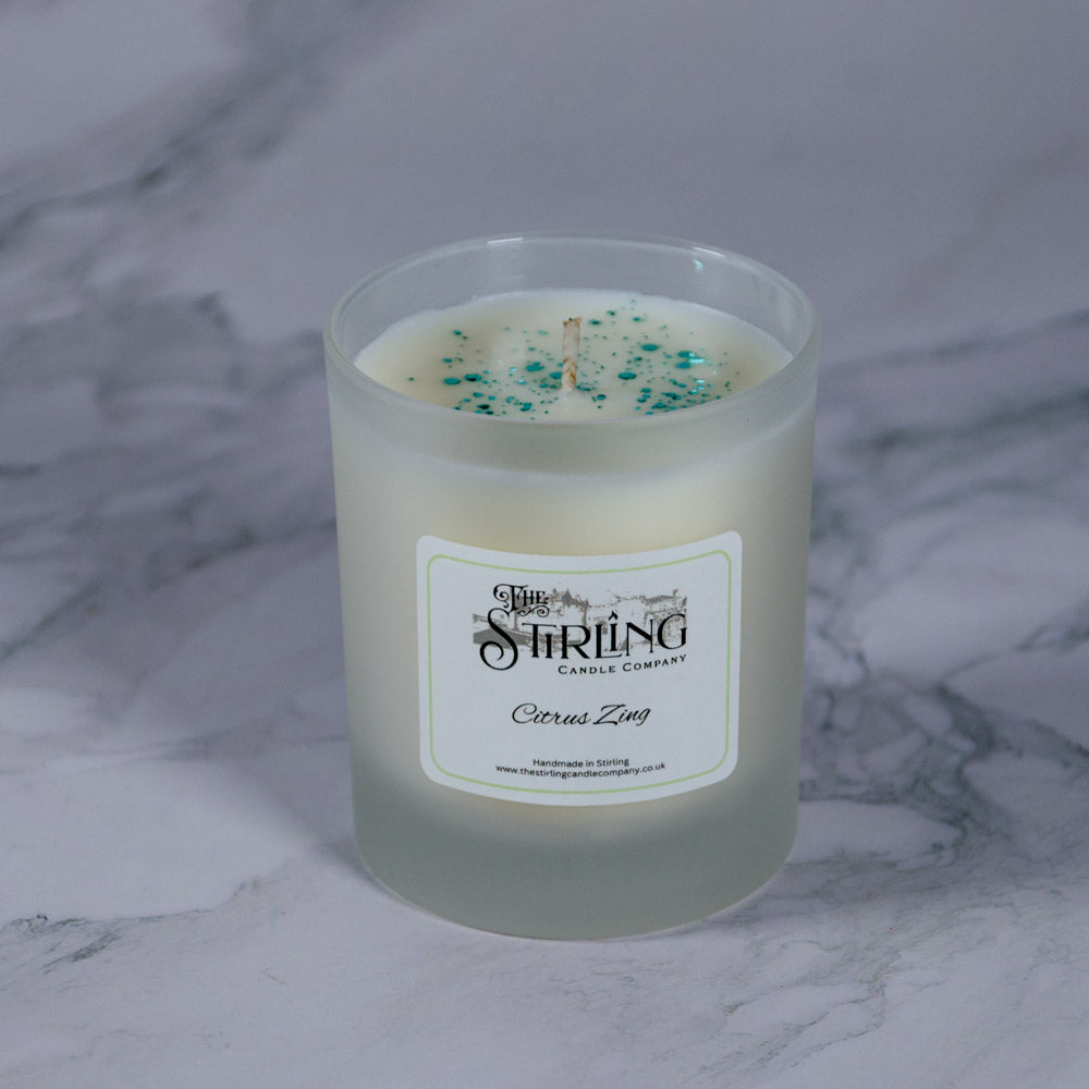 A frosted glass medium candle jar with white wax and teal glitter sprinkles labeled citrus zing by stirling candle company