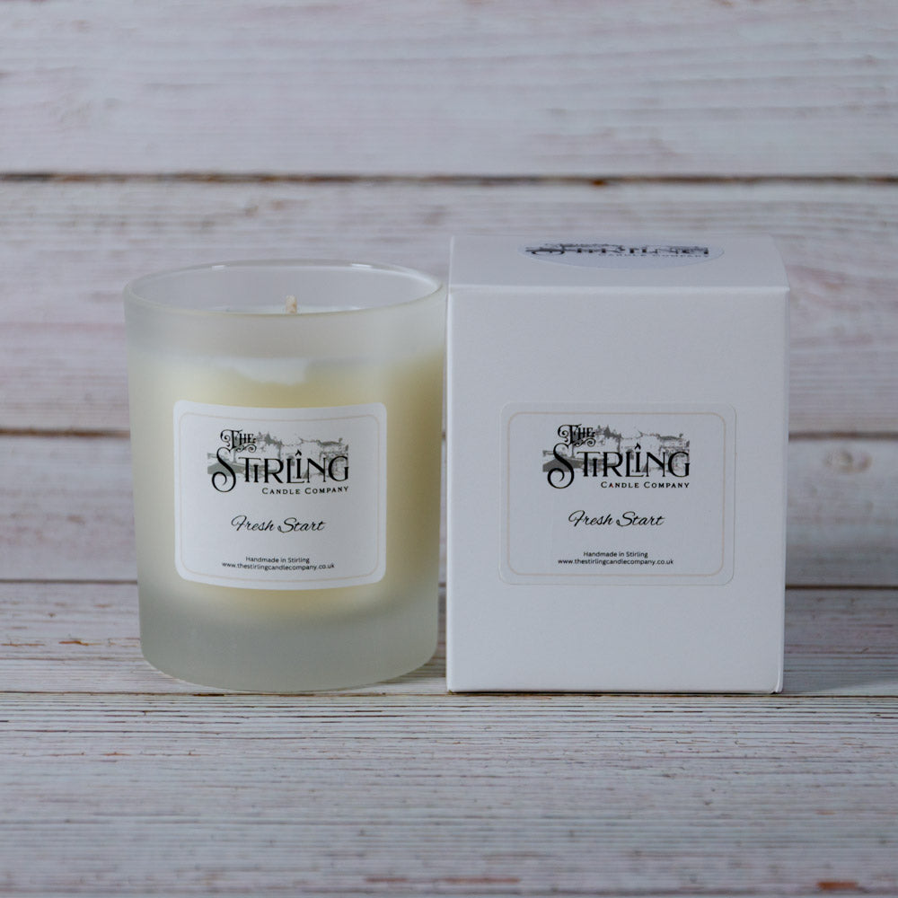 A frosted glass candle jar with creamy white wax and a fresh start label from stirling candle company medium candle