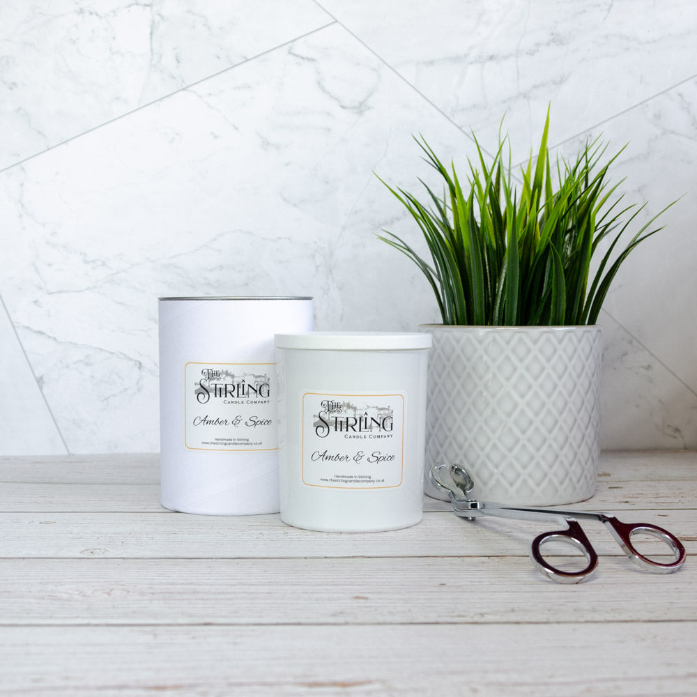 Two white cylindrical amber and spice scented candles from the stirling candle company on a wooden surface