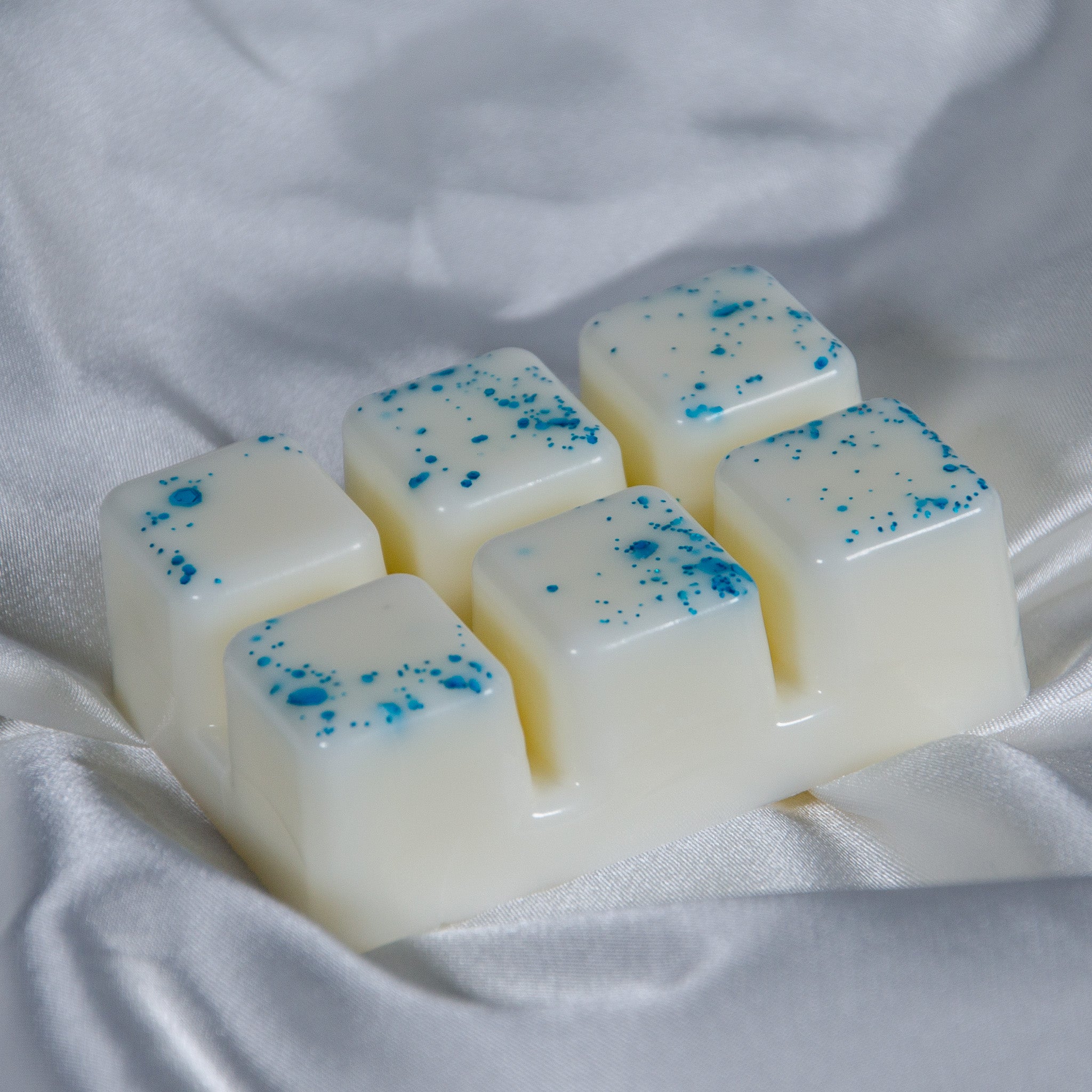 Six square-shaped white wax melts with blue speckles in a tray fairy dust wax melt clamshell