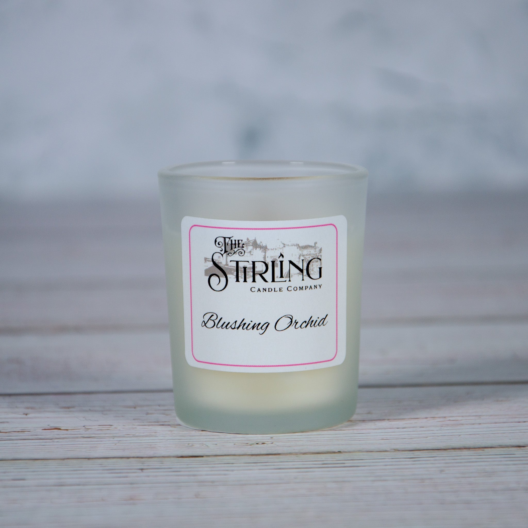 A frosted glass candle jar with a white label featuring pink trim from the stirling candle company blushing orchid scent
