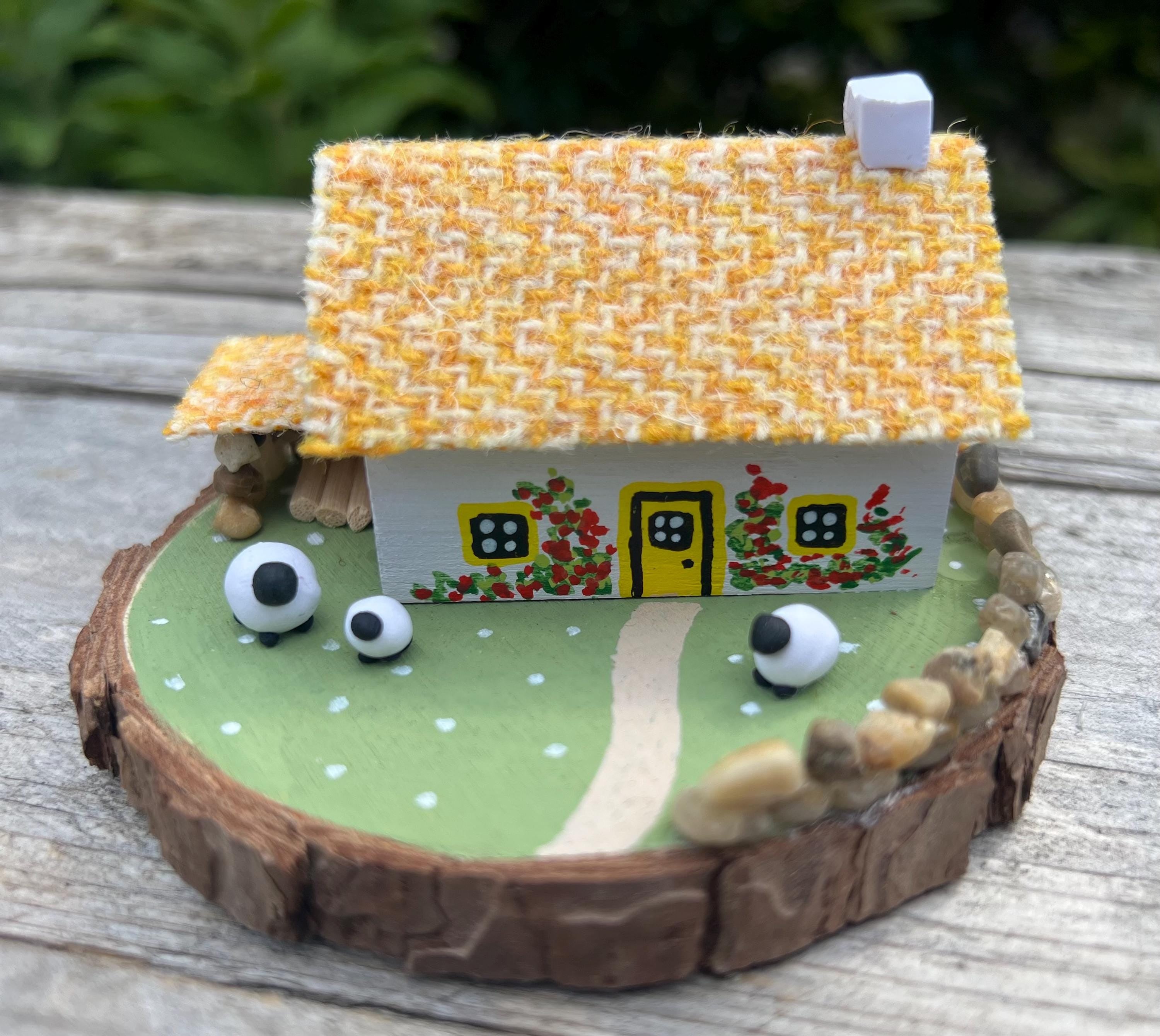 Miniature handcrafted Scottish Bothy with yellow thatched roof, painted roses, sheep, and green lawn